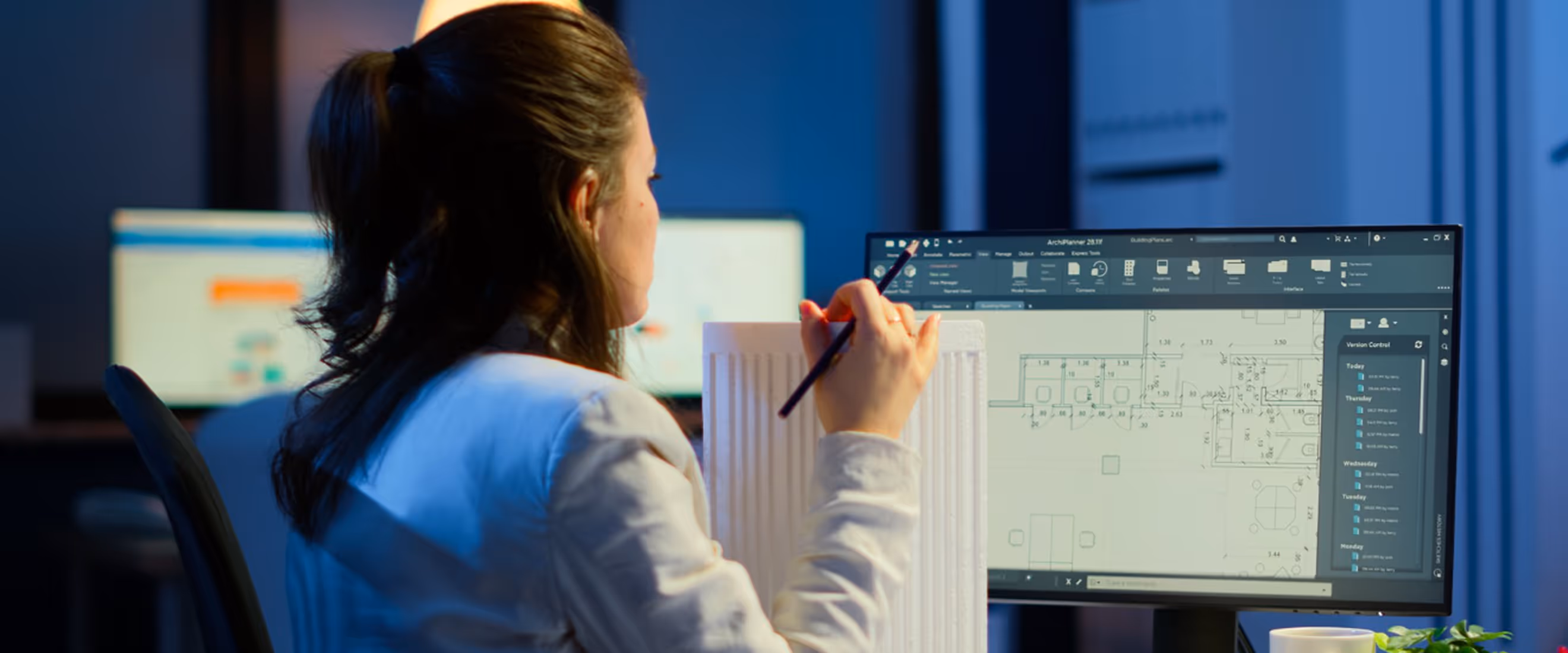 Woman in white shirt working on architectural design displayed on a computer monitor.