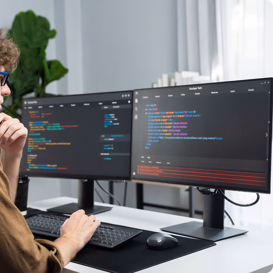 Person working with two monitors displaying colorful computer code in a modern office setup.