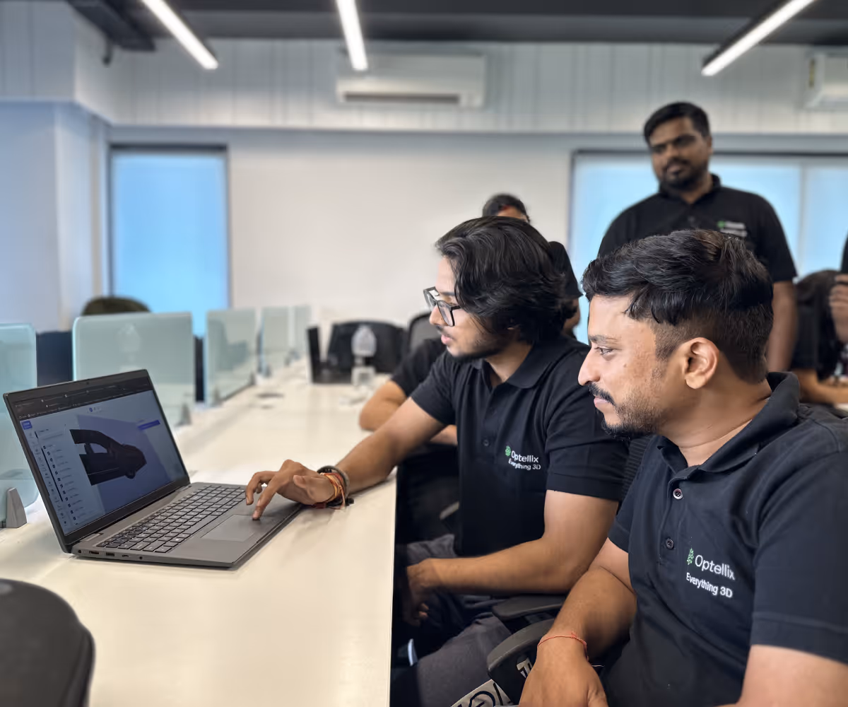 Two men in black Optellix shirts working on a 3D design on a laptop in a modern office.